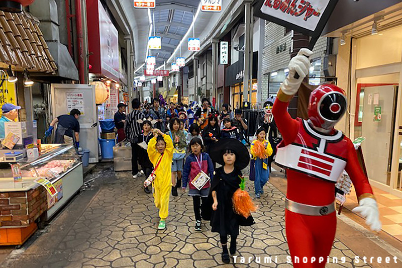 仮装したみんなで商店街をパレード。先頭には垂水のヒーロー「たるみんジャー」。後ろには須磨のスターしんごお兄さんもいます